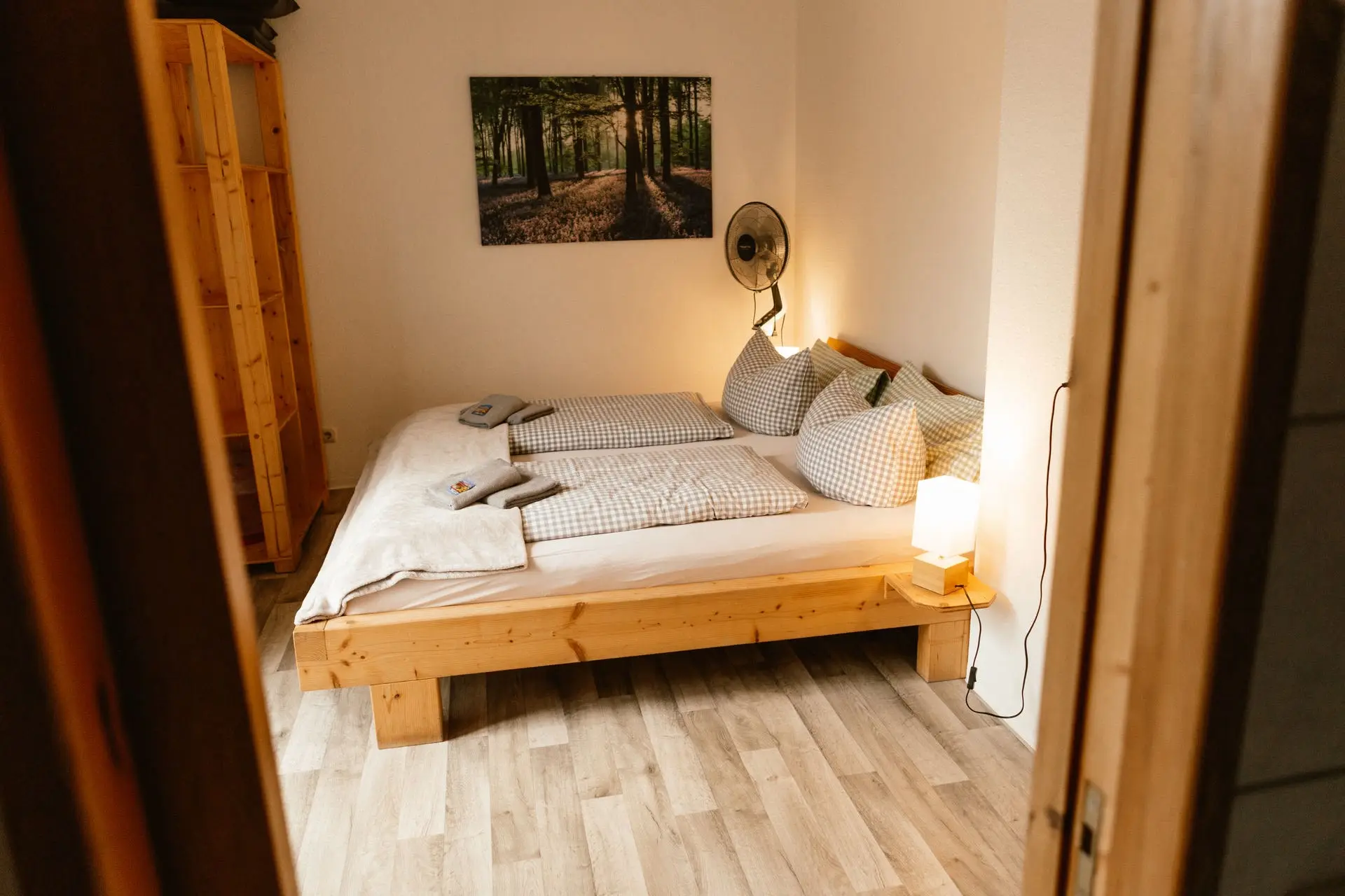 Doppelzimmer: Massivholzbett mit karierter Bettwäsche und warmem Abendlicht