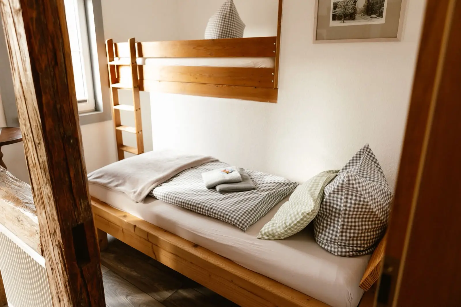 Einzelzimmer: Bett mit karierter Bettwäsche in der Holznische, darüber ein Hochbett