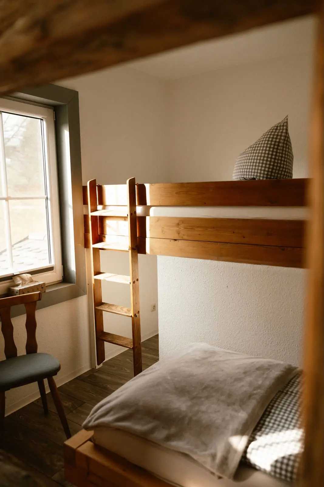 Einzelzimmer: Blick auf Bett, Stuhl und Sprossenfenster mit Morgenlicht