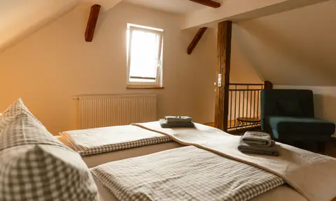Familien-Suite: Schlafbereich unter historischen Dachbalken mit Galerie und Sessel